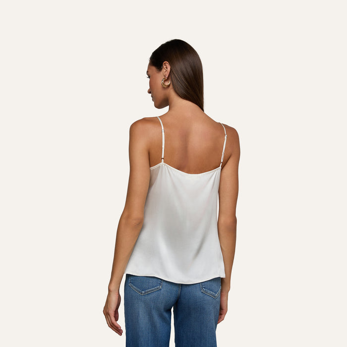 A woman with straight brown hair is facing away, wearing the Gabriella Silk Camisole in ivory with thin straps and blue jeans. The background is plain and light-colored.