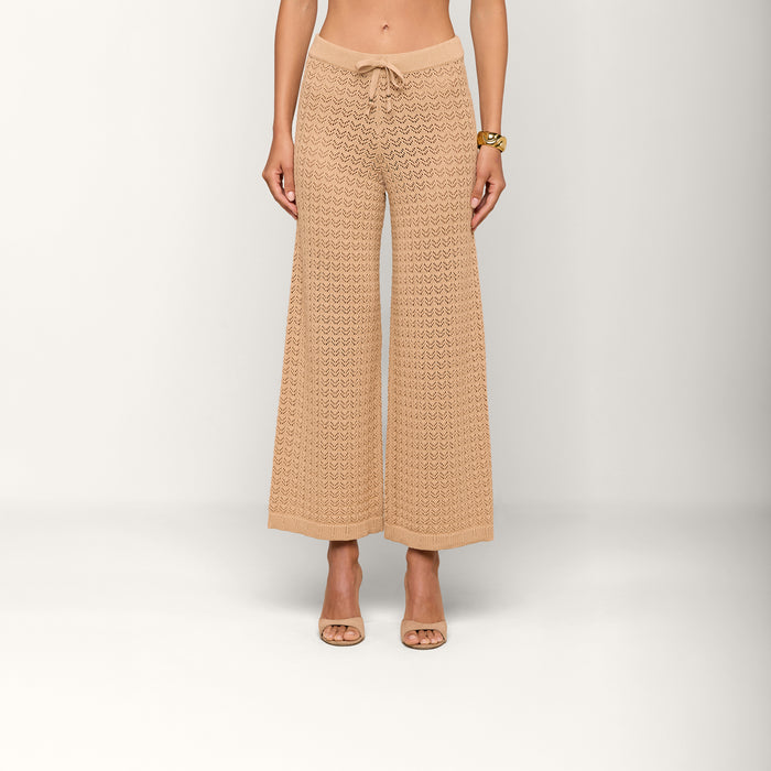 A woman, shown from the midriff down, wears the beige Gaelle Pointelle Knit Pant featuring a crocheted design and drawstring waist, paired with open-toe heels against a plain white background. The lightweight style is ideal for vacation.