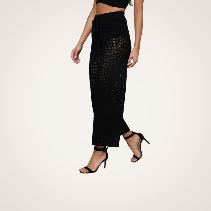 Model wearing the black Gaelle Pointelle Knit Pant, featuring a wide-leg silhouette and drawstring waist, styled with high heels; shown from mid-torso down against a plain light background.