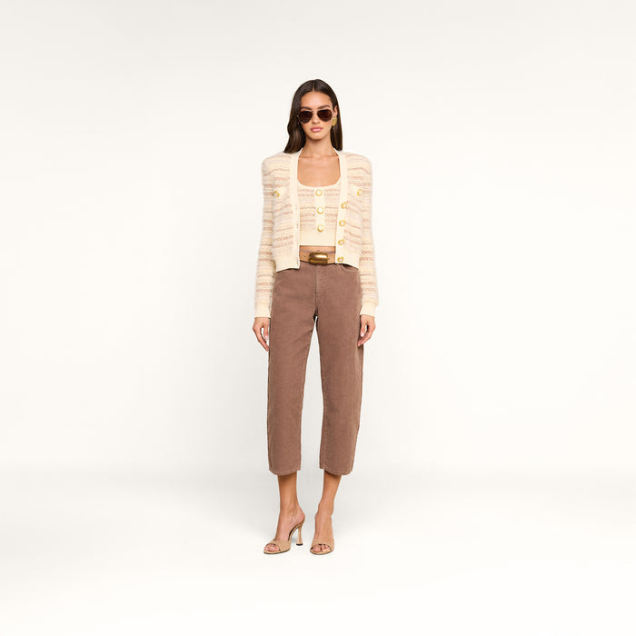 A woman wearing sunglasses, a beige striped cardigan with decorative buttons over the Galene Tank, brown cropped pants, and beige high-heeled sandals stands against a plain white background.