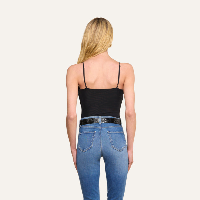A woman with long blonde hair, wearing the Gelina Mesh Bodysuit with adjustable straps and blue jeans with a black belt, stands facing away from the camera against a plain light background.