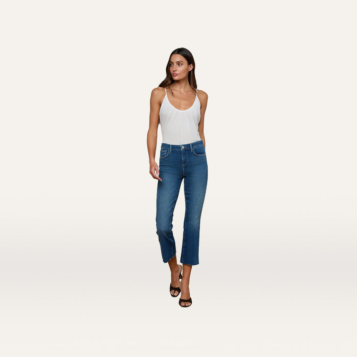 A woman wearing the Gelina Ruched Bodysuit with adjustable straps, paired with blue cropped jeans and black heels, stands against a plain white background looking slightly to her left.