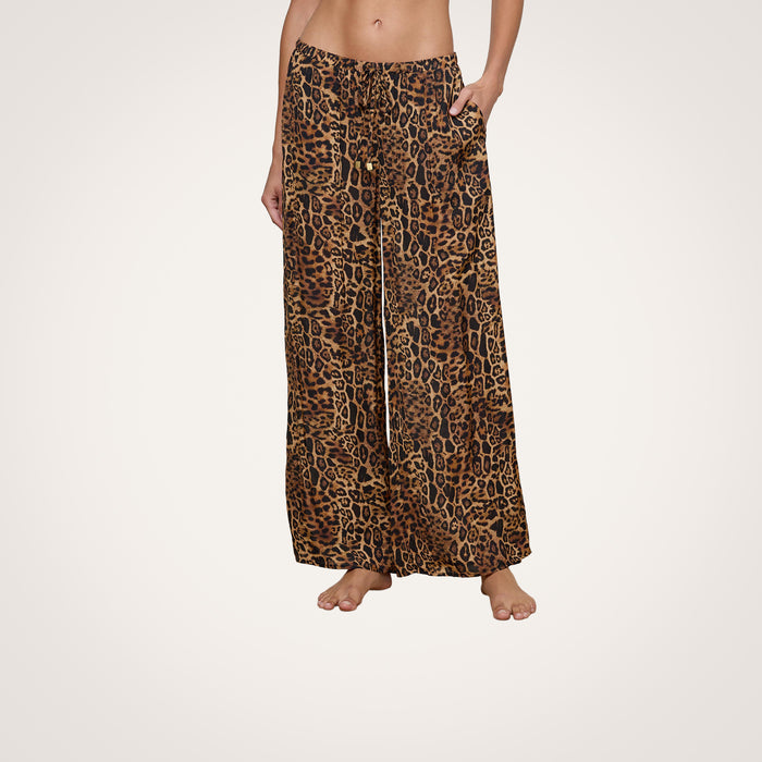 A person wearing the Geraldine Cover-Up Pant—a loose, wide-leg style with a brown and black leopard print and a comfortable pull-on fit—stands barefoot against a plain white background, embodying effortless resort wear.