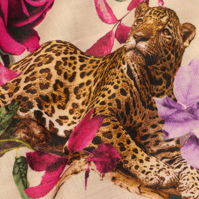A close-up of the Geraldine Cover-Up Pant fabric, showcasing a relaxed leopard surrounded by purple and pink flowers on a beige rose leopard print background.