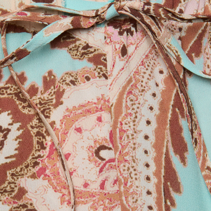 Close-up of the Geraldine Cover-Up Pant, featuring fabric with a paisley print in shades of brown, pink, and cream on a light blue background; a thin fabric tie near the top adds to its effortless resort wear style.