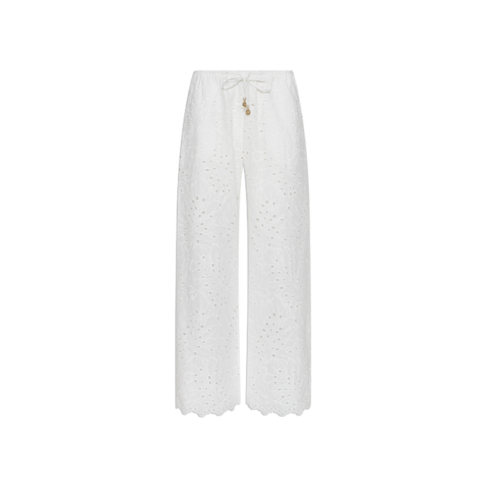 The Geraldine Eyelet Cover-Up Pant features a white, wide-leg silhouette crafted from cotton eyelet, complete with scalloped hems and a tie waist accented by small decorative charms—making it perfect for resort wear. Shown against a plain white background.