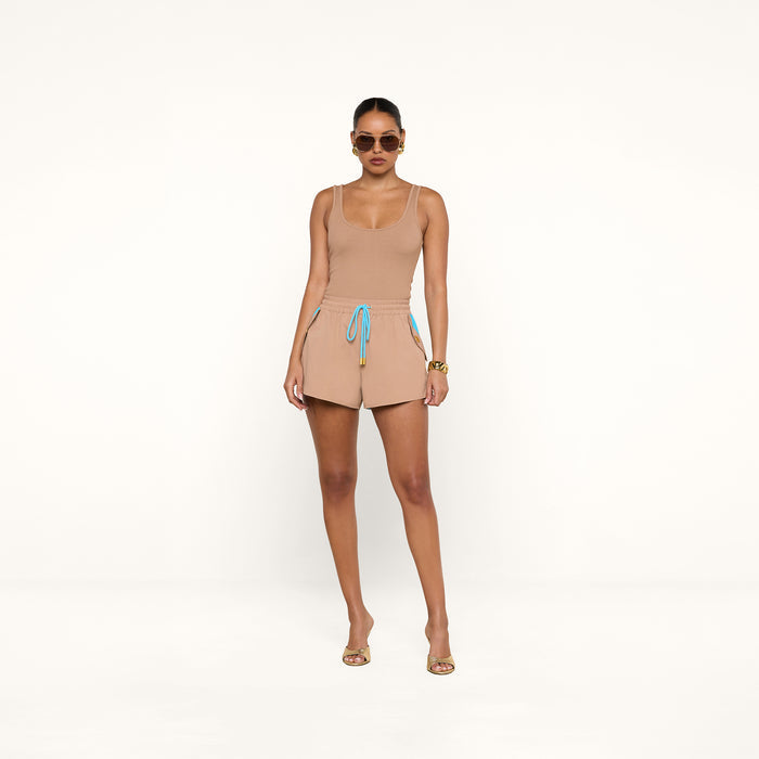 A woman in sunglasses wears a beige tank top and the Grayson Nylon Short, featuring a blue and yellow drawstring and crafted from water-repellent crepe nylon, standing against a plain white background.