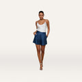 Woman wearing a white camisole, Hadleigh Linen-Blend Short in dark blue with a high rise, and silver heels, standing with hands in pockets against a plain white background.