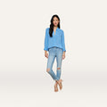 A woman stands against a plain background, wearing a light blue button-up shirt paired with the High Line Distressed Skinny Jean in a vintage wash with rips, and beige heeled sandals. She has long black hair and her arms are relaxed at her sides.