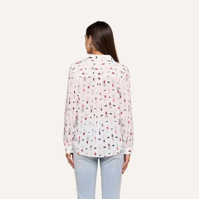 A woman with long brown hair is shown from the back against a plain light background, wearing the Holly Blouse—a slim fit, long sleeve button-down shirt featuring a red and black geometric print—paired with light blue jeans.