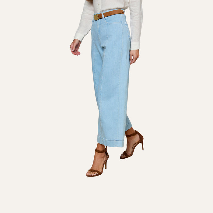 A person is wearing the Houston Cropped Wide-Leg Jeans in light blue stretch denim, paired with a white long-sleeve shirt, a brown belt, and brown high-heeled sandals. Only the lower half of their body is visible against a plain light background.