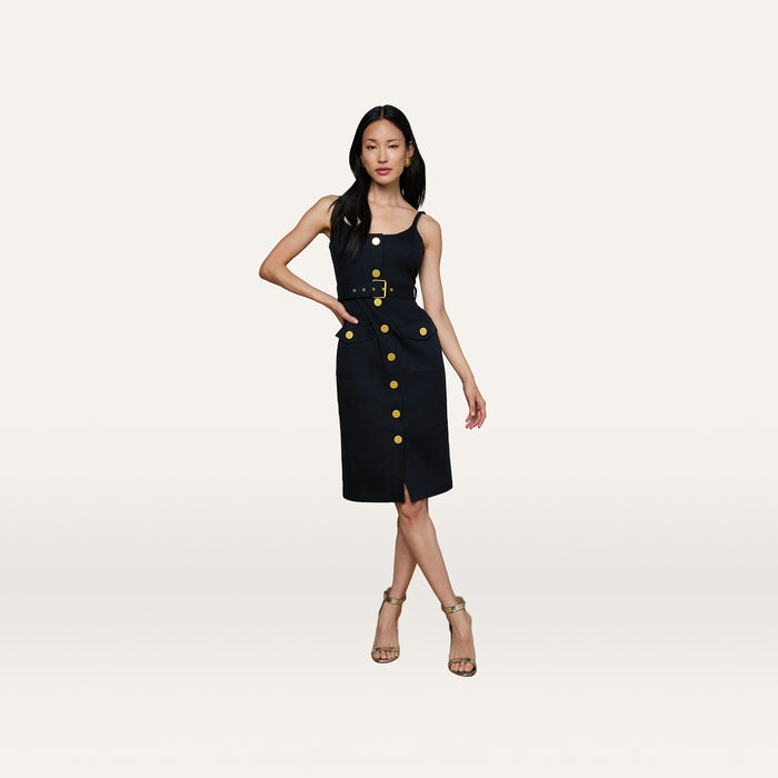 A woman poses in the Ida Dress, a sleeveless, knee-length dress featuring gold buttons and a belted waist, styled with strappy heels against a plain white background.