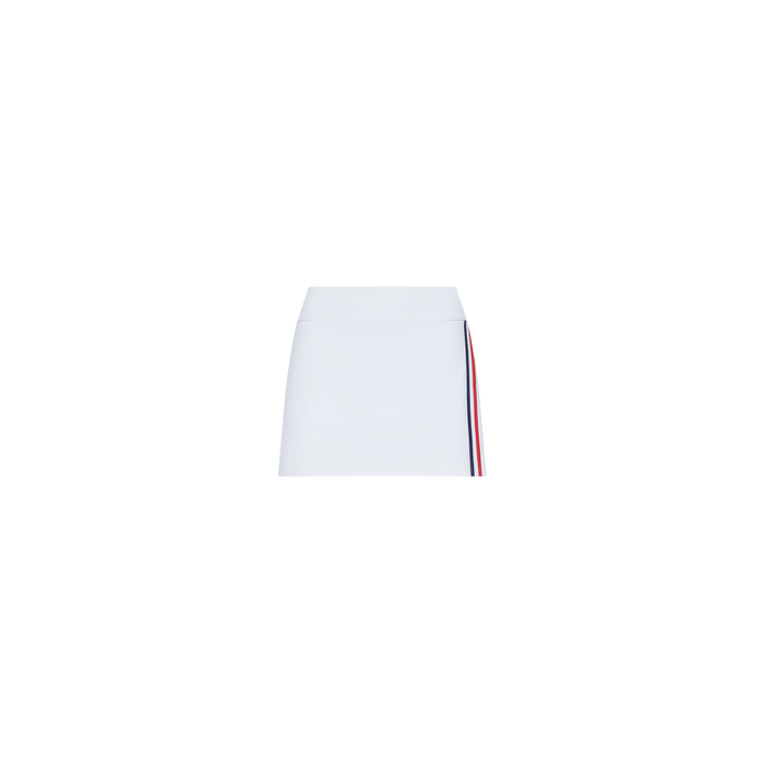 The Iga Tennis Skort is a white mini tennis skirt with a simple design, featuring a vertical red and navy blue stripe along one side, displayed against a plain white background.