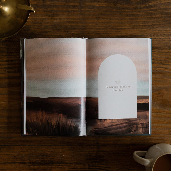 In the Grips of His Grace Study opened to a full page image with a small excerpt about remaining faithful, on a brown wooden table next to a bronze oil lamp and a white coffee cup