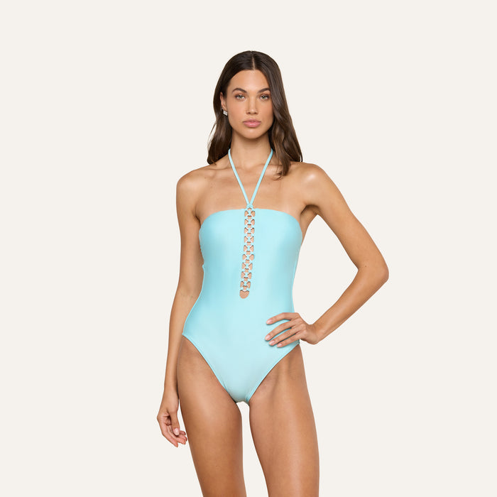 A woman wearing the Indore One-Piece Swimsuit in ice blue, featuring a strapless design with a halter neck and decorative cutout details down the front, stands against a plain light background.