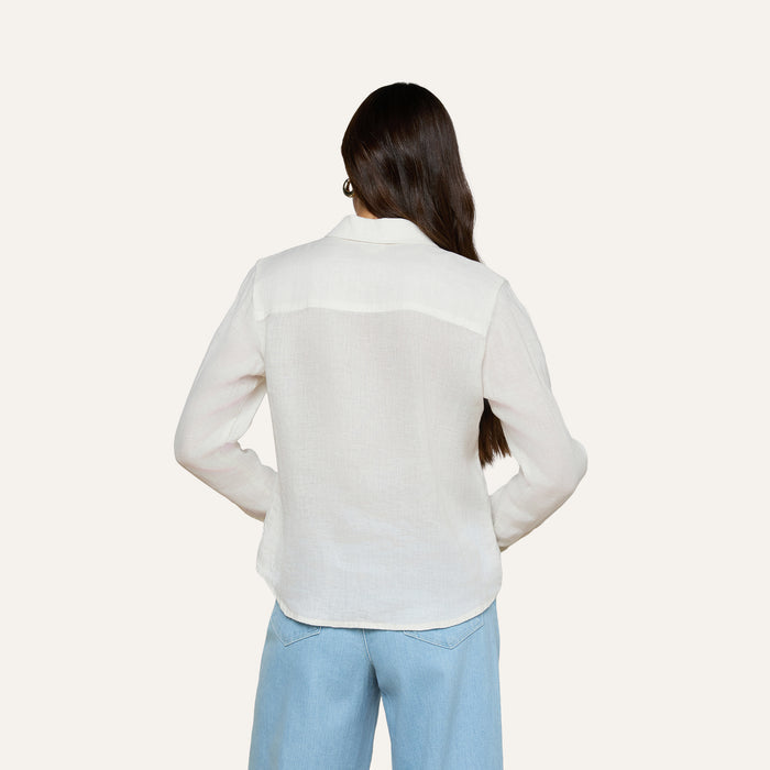 A person with long brown hair is shown from the back, wearing the Isla Linen Shirt in white and light blue jeans, against a plain light background.