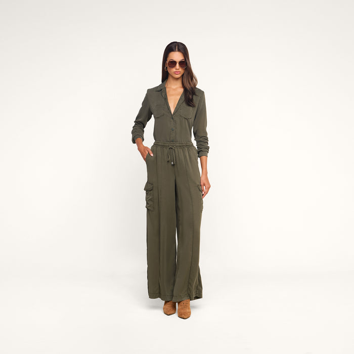 Woman in sunglasses wears the Isla Shirt, a featherweight twill olive green long-sleeve shirt with wide-leg pants, standing with one hand in her pocket against a plain white background.