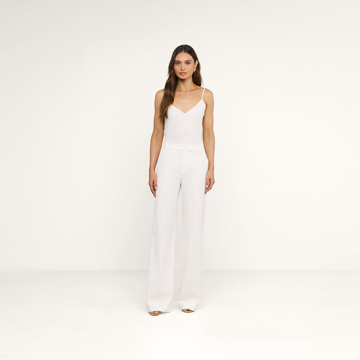 A woman stands facing forward, layering the Jane Silk Camisole with adjustable straps under a sleeveless white jumpsuit with wide-leg pants and open-toe shoes against a plain white background.