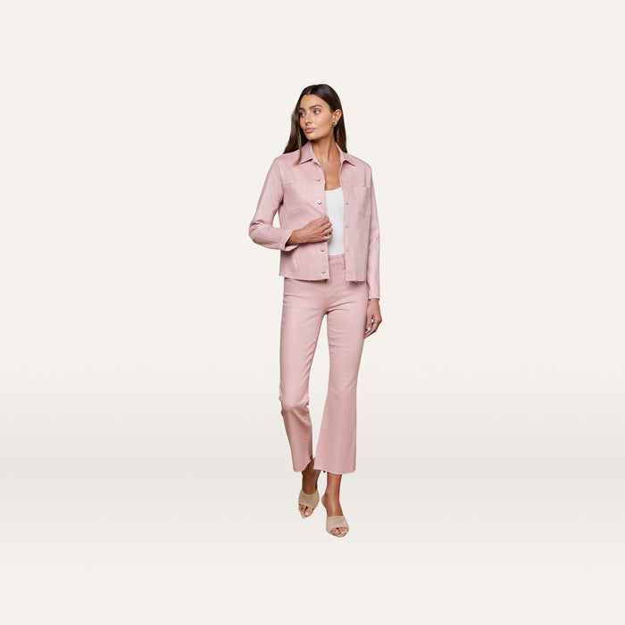 A woman stands against a plain white background, wearing the Janelle Coated Jean Jacket in light pink with matching pants over a white top. She has long hair and is wearing open-toed heels.