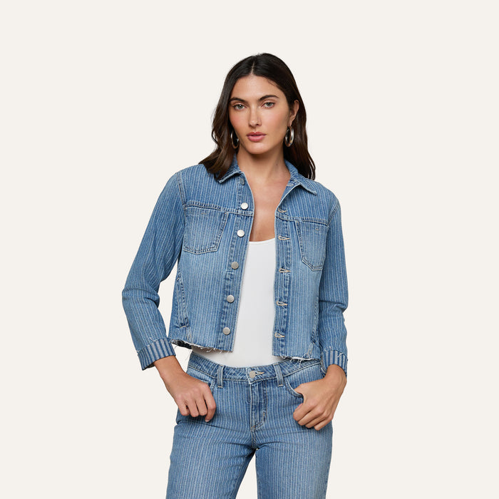 A woman wears the slim-fit Janelle Jean Jacket in all-cotton pinstriped indigo over a white top, paired with matching pinstriped jeans, standing against a plain light background.