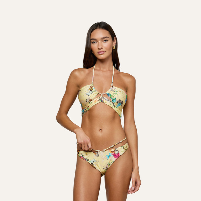 Woman wearing the Jean Bikini Bottom, a yellow floral high-leg cut style, paired with a matching halter-style wrap top, posing against a plain light background.