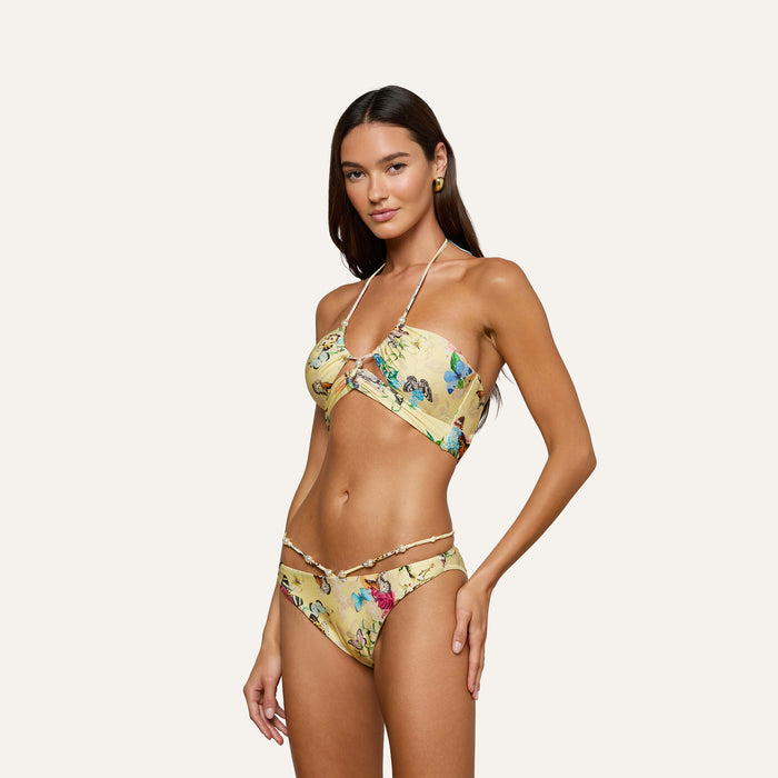 Model wearing the Jean Bikini Bottom—a yellow floral, high-leg cut bikini with halter straps—posing against a plain, light background.