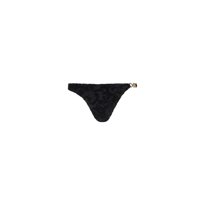 The Jean Bikini Bottom is a timeless black thong bikini bottom with a subtle floral pattern and decorative gold detail on the left hip, featuring a flattering high-leg cut, displayed on a plain white background.