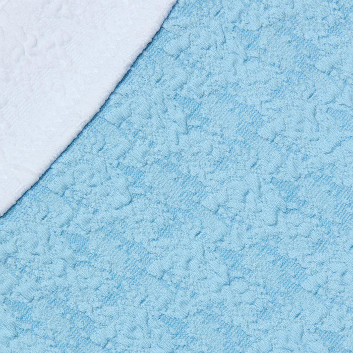 A close-up of the Jean Bikini Bottom in a textured light blue bouclé fabric, with a white towel overlapping it diagonally in the upper left corner.