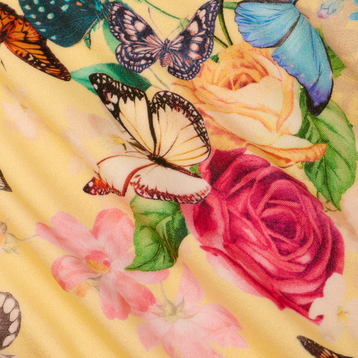 The Jean Bikini Bottom features a yellow fabric adorned with a vibrant butterfly print, showcasing colorful butterflies and an array of flowers—including pink lilies and a red rose—for a detailed, lively springtime look.