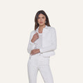 A woman stands against a plain background, wearing the Celine Jean Jacket in optic white with a relaxed fit, layered over a matching shirt and white jeans. She has straight brown hair and a neutral expression, with one hand touching the jacket near the collar.