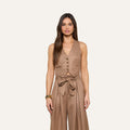 Wearing the Jianna Vest, a woman with long brown hair poses against a plain light background, pairing the minimalist tan button-up vest with matching high-waisted, wide-leg pants tied with a bow belt.