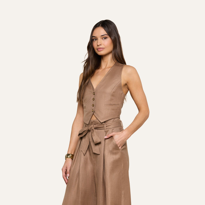 A woman wears the sleeveless, minimalist Jianna Vest with buttons and matching high-waisted, wide-leg trousers featuring a tied belt, standing against a plain light background.