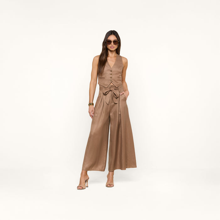 Woman wearing sunglasses, the Jianna Vest—a sleeveless linen style—wide-leg high-waisted pants with a bow belt, and heeled sandals stands against a plain white background.