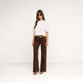 A woman wearing sunglasses, a white short-sleeve top, the Joanne Low-Rise Wide-Leg Jean with a belt, and brown heels stands against a plain white background.