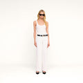 A woman stands against a plain white background, wearing black sunglasses, a white tank top, the Joanne Low-Rise Wide-Leg Jeans with a black belt and black heels.