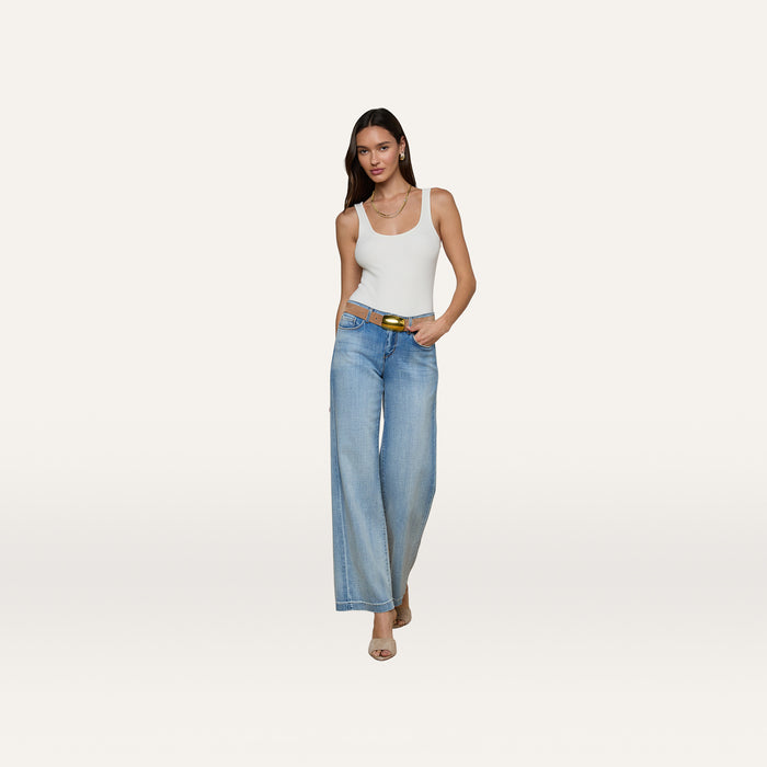 A woman wearing a white tank top, beige heels, and a belt stands against a plain white background in light blue Joanne Low-Rise Wide-Leg Jeans.
