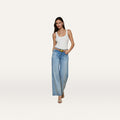 A woman wearing a white tank top, beige heels, and a belt stands against a plain white background in light blue Joanne Low-Rise Wide-Leg Jeans.