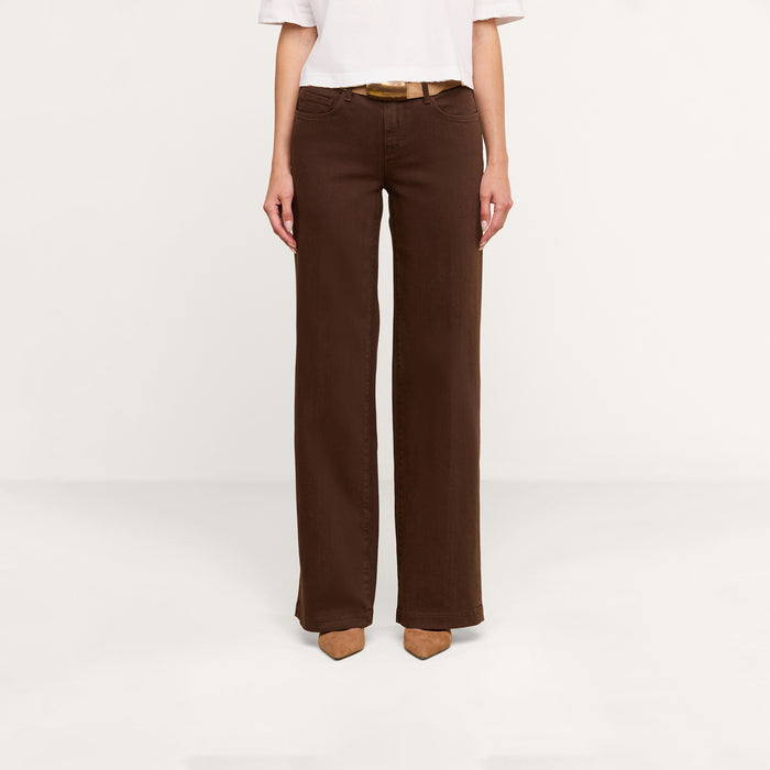 A person wearing the Joanne Low-Rise Wide-Leg Jean in dark brown, paired with a white top and brown pointed-toe shoes, stands against a plain white background.
