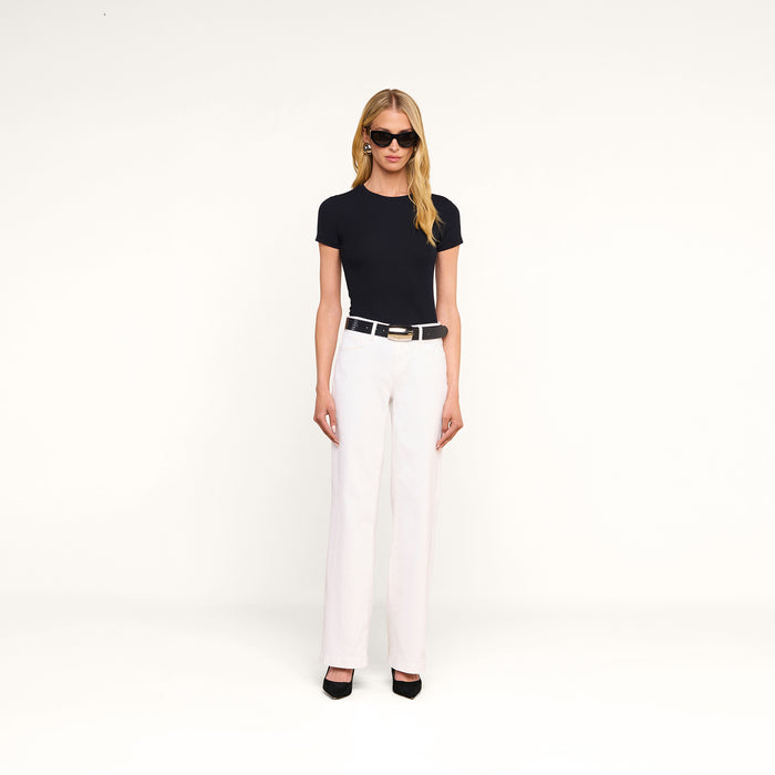A woman wearing sunglasses, a black t-shirt, the Joanne Low-Rise Wide-Leg Jean, and black heels stands against a plain white background.
