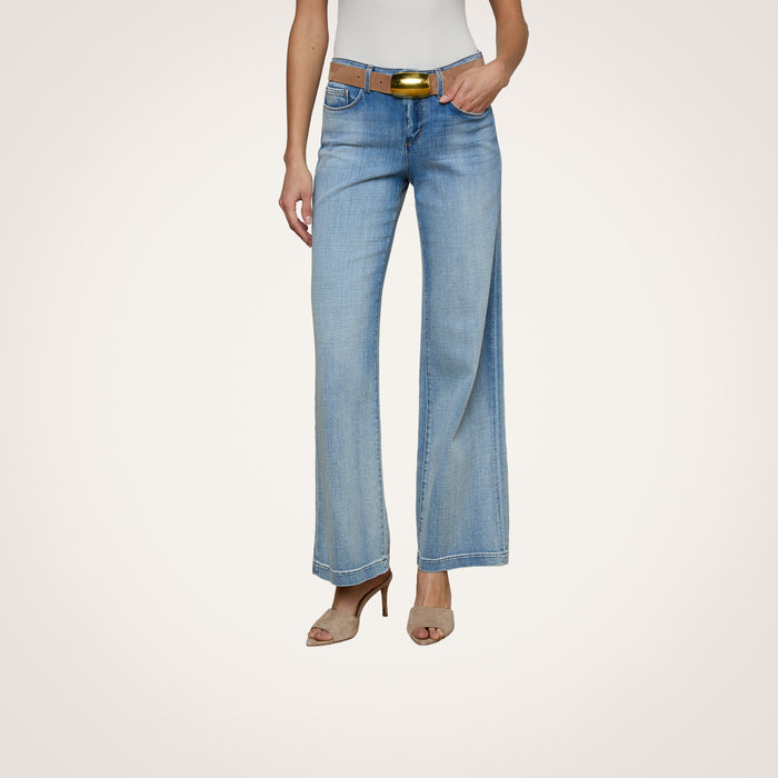 A woman wears the Joanne Low-Rise Wide-Leg Jean in light blue, paired with a brown belt, white sleeveless top, and beige heeled sandals. She stands against a plain light background with only the lower half of her body visible.