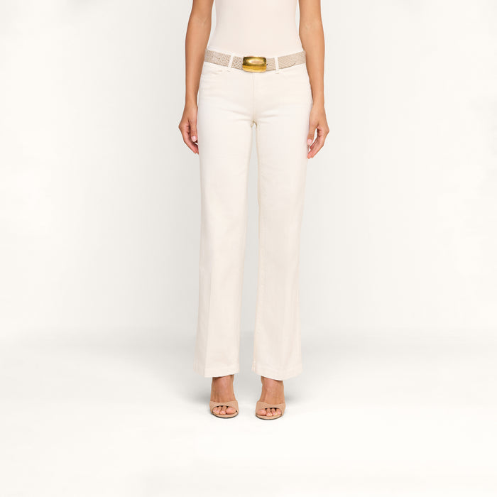 A woman wearing Joanne Low-Rise Wide-Leg Jeans in an ecru wash, paired with a beige sleeveless top, a textured belt with a gold buckle, and beige open-toe heels stands against a plain white background.