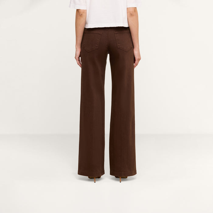A person stands facing away, wearing a cropped white shirt and the Joanne Low-Rise Wide-Leg Jean in dark brown with back pockets, against a plain white background.