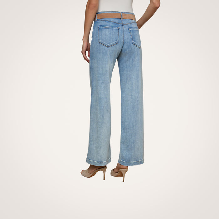 A person shown from the back against a plain background wears the Joanne Low-Rise Wide-Leg Jean in light blue, styled with exposed hips and high heels.