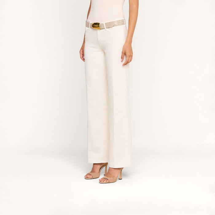 A person is shown from the waist down wearing the Joanne Low-Rise Wide-Leg Jean in an ecru wash, paired with a beige sleeveless top, a textured light belt featuring a gold buckle, and open-toed heels, standing against a plain white background.