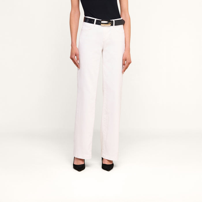 A person stands against a white background wearing the Joanne Low-Rise Wide-Leg Jean, paired with a black belt, black top, and black heels. Their arms are relaxed by their sides and their head is not visible in the image.