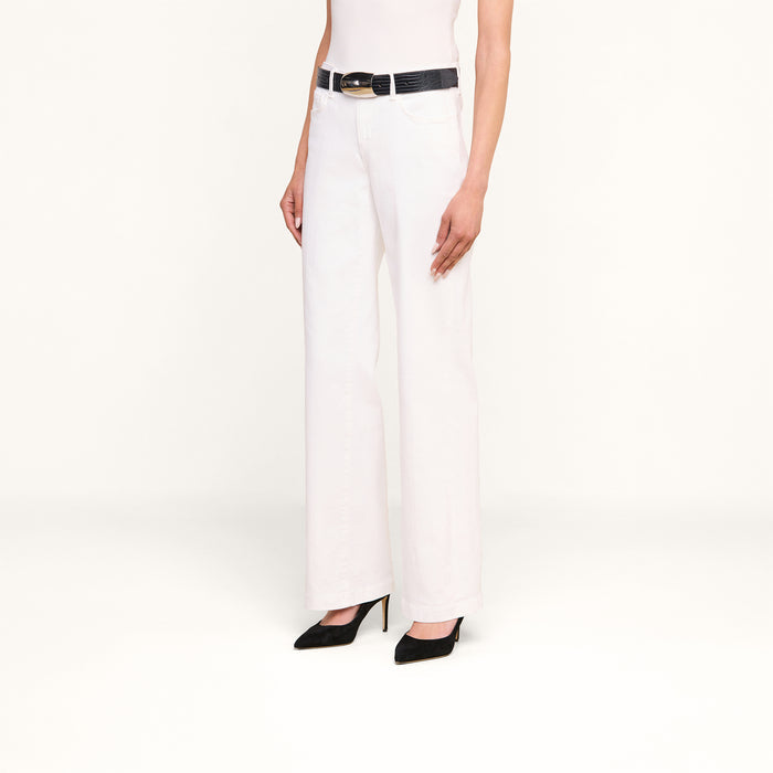 Wearing the Joanne Low-Rise Wide-Leg Jean in a white wash, styled with a black belt and black pointed-toe heels, the person is standing against a plain white background with their torso and legs visible.