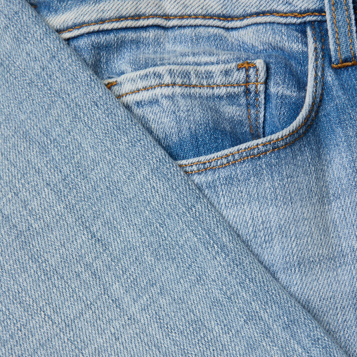 Close-up of the Joanne Low-Rise Wide-Leg Jean in light blue stretch denim, showing a front pocket and detailed stitching, with a diagonal section of denim fabric overlapping the jeans.