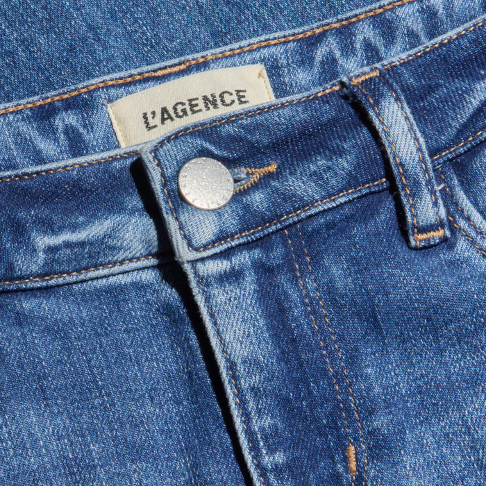 Close-up of blue denim Joanne Low-Rise Wide-Leg Jeans featuring a silver button, orange stitching, and a visible white clothing label with LAGENCE printed in black. Crafted from stretch denim, these jeans combine comfort with classic style.