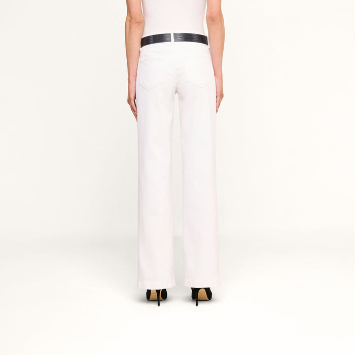 Person standing facing away, wearing Joanne Low-Rise Wide-Leg Jeans with a black belt and black high heels, against a plain white background. Only the lower half of the body is visible.