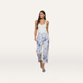 A woman wearing a sleeveless white top and the June Cropped Stovepipe Jean — a high-rise, straight-leg white pant with blue floral paisley print — paired with light blue heeled sandals, stands against a plain background.